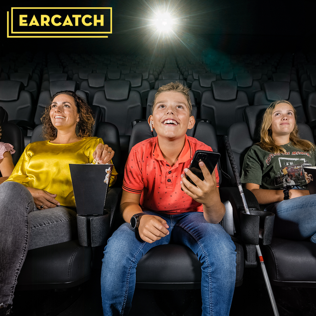 Een gezin kijkt in de bioscoop lachend voor zich uit. De jongen in het midden heeft een telefoon in zijn hand en een draadloos oortje in zijn oor. Links van hem staat een blindenstok. In de linkerbovenhoek staat het gele logo van Earcatch.